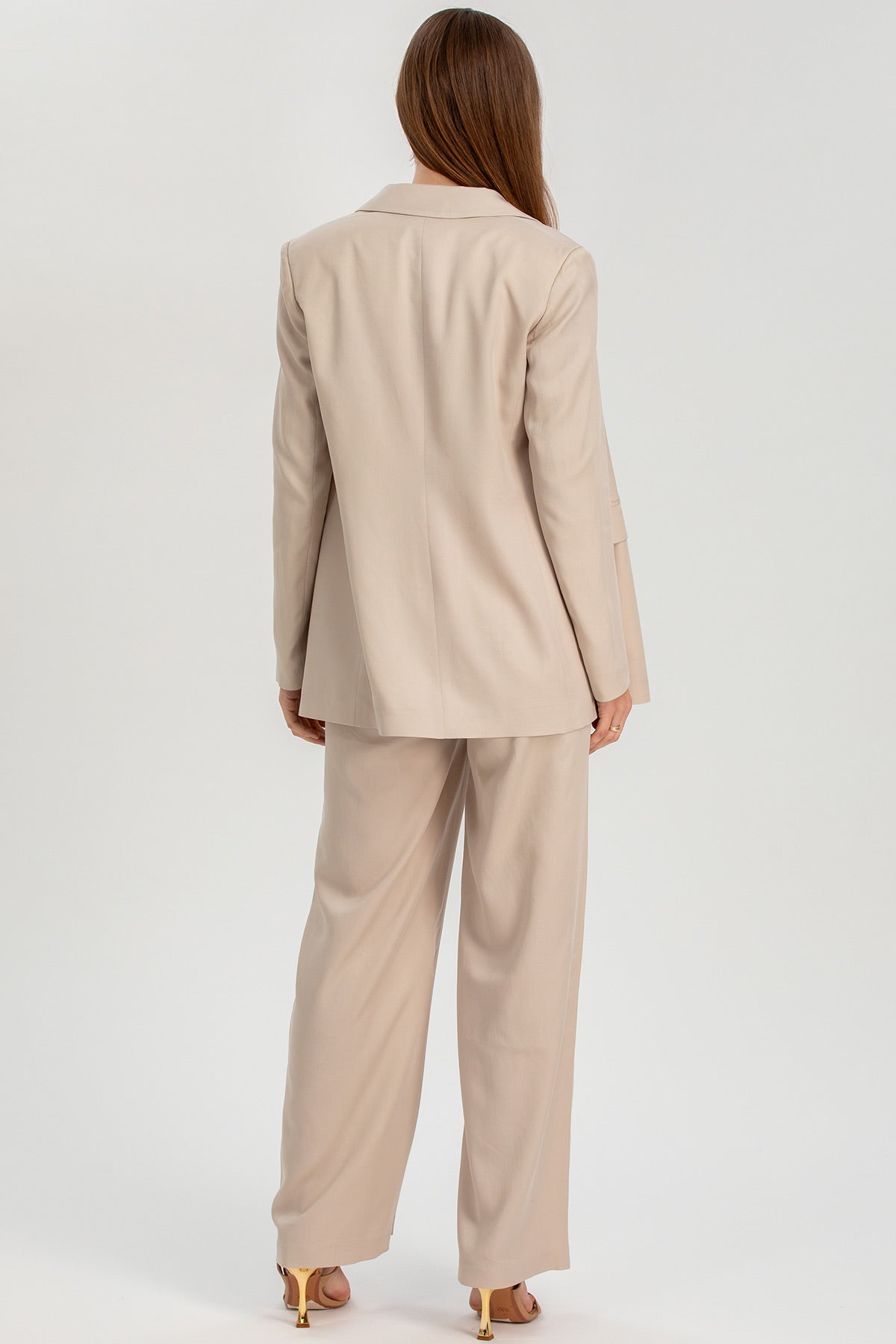 Donna di spalle con tailleur premaman beige elegante e tacchi dorati