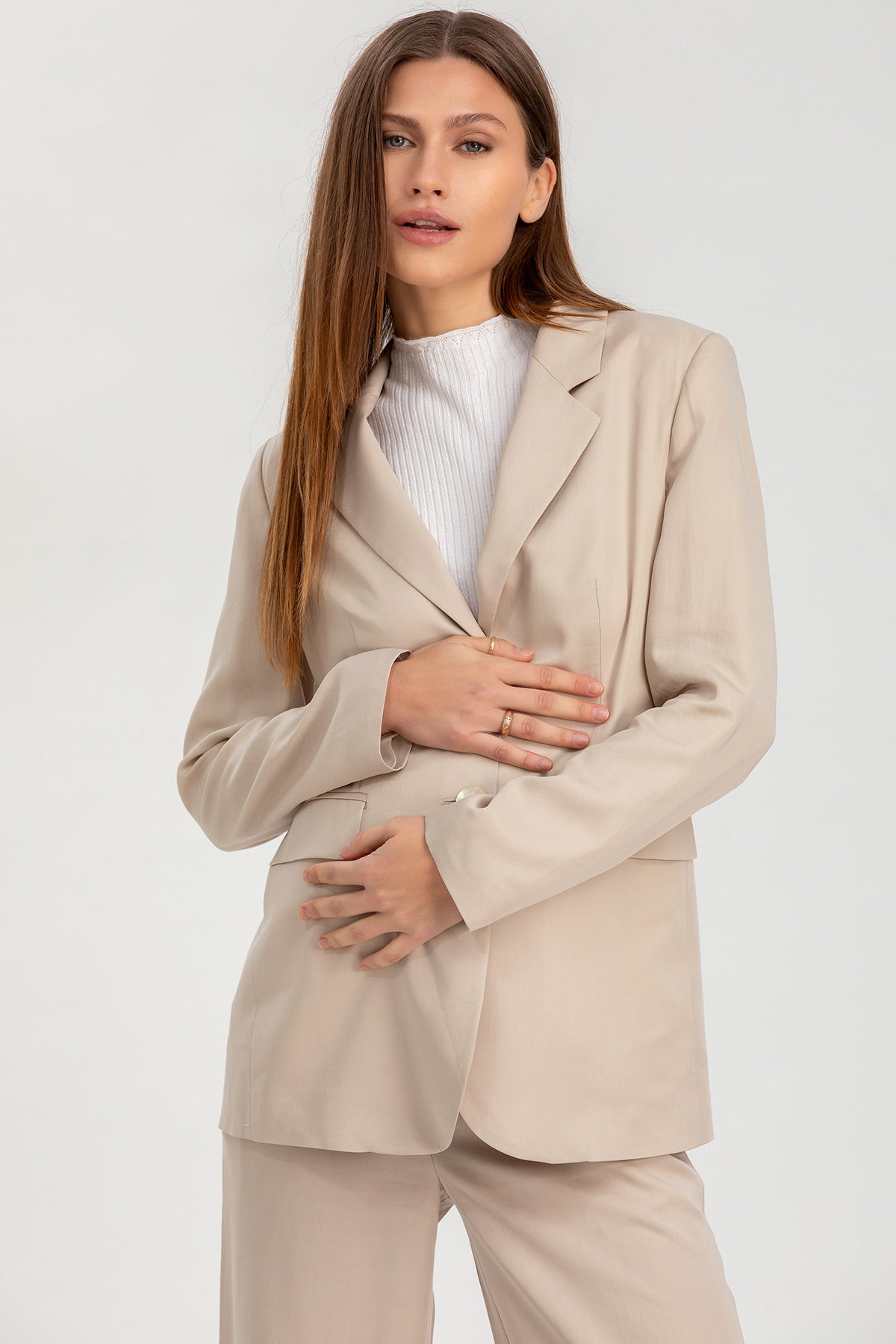 Donna incinta con completo pantalone premaman beige elegante, camicia bianca, fondo neutro