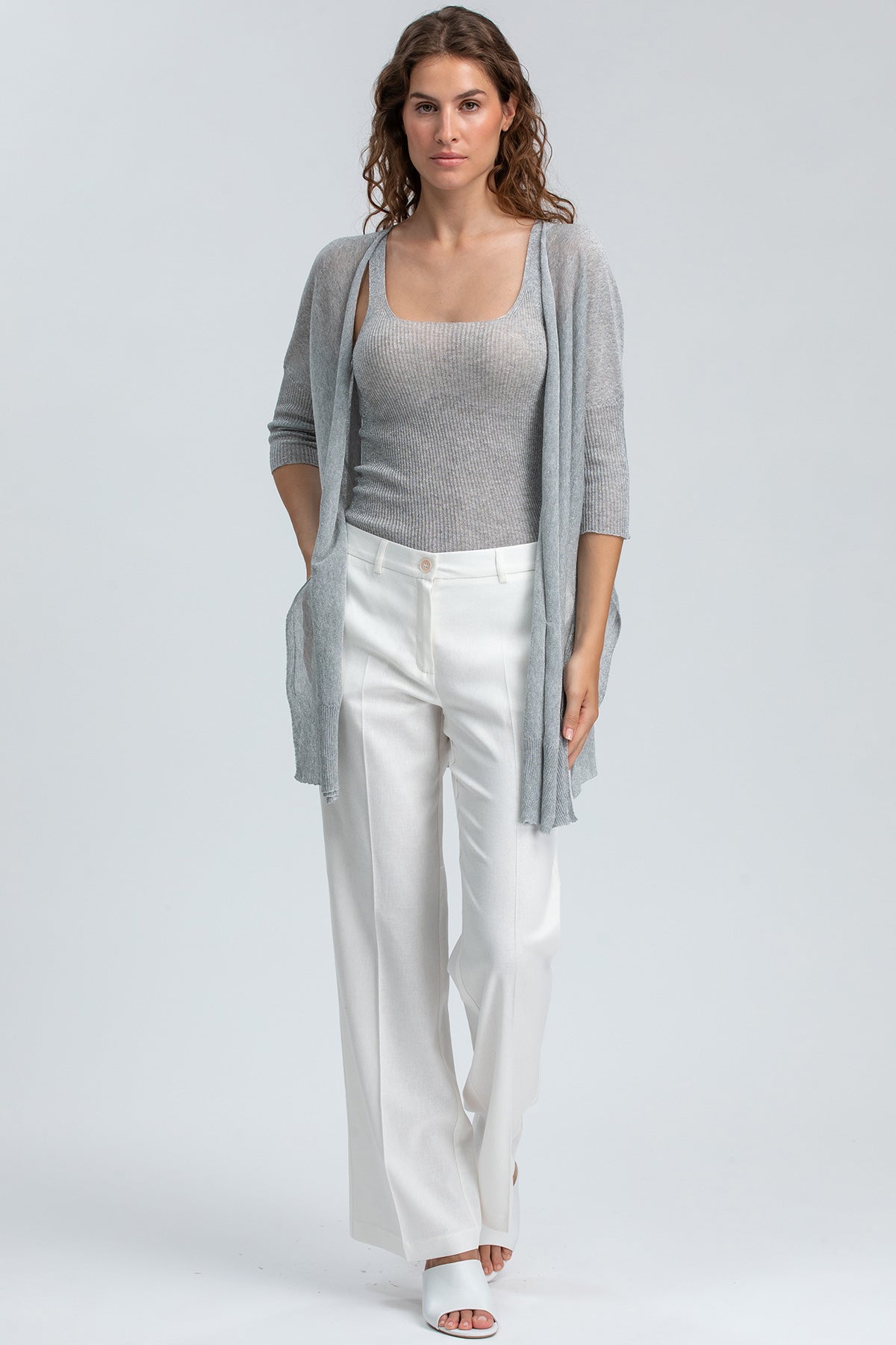 Modella indossa cardigan grigio e pantaloni bianchi premaman eleganti su sfondo neutro