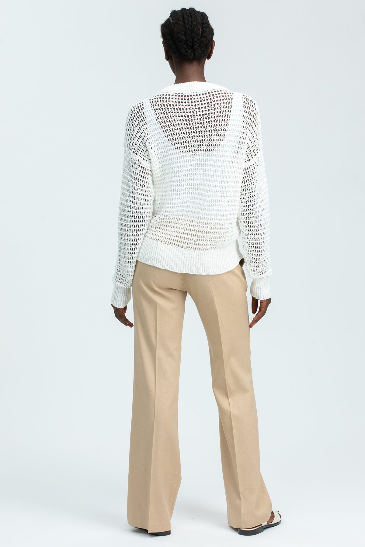 Donna di spalle con maglione premaman traforato bianco e pantaloni beige eleganti.