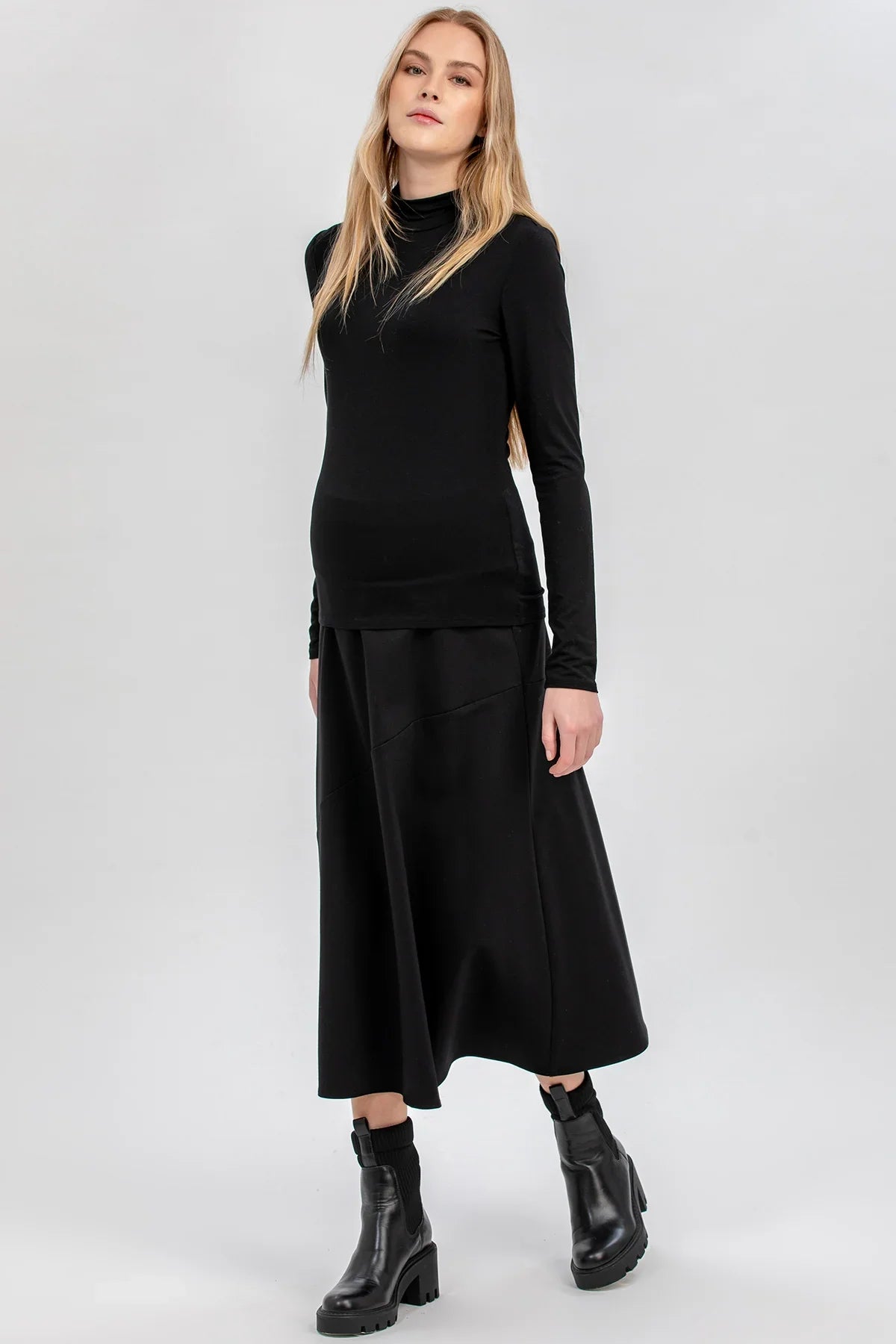 Modella indossa abbigliamento premaman nero elegante con maglia a maniche lunghe e gonna midi.