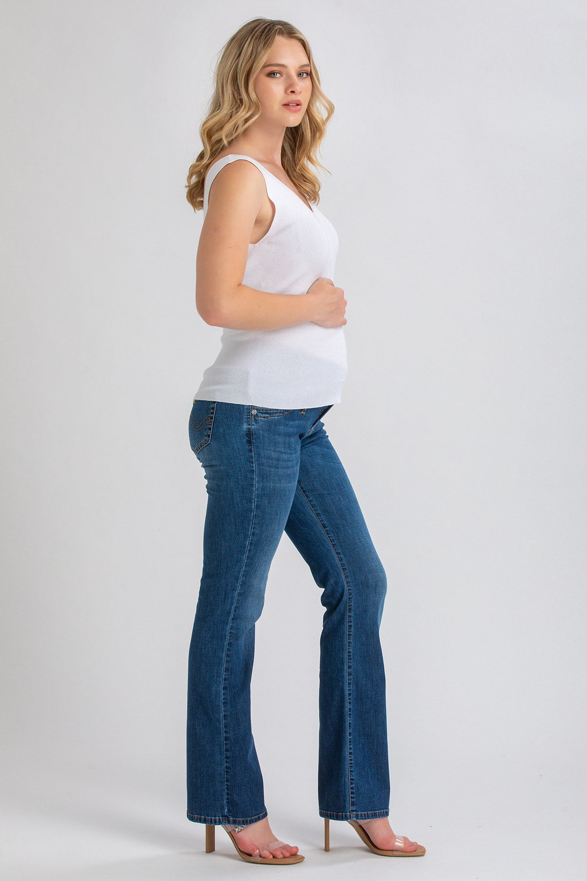 Donna incinta con top bianco e jeans premaman bootcut blu in studio, moda gravidanza