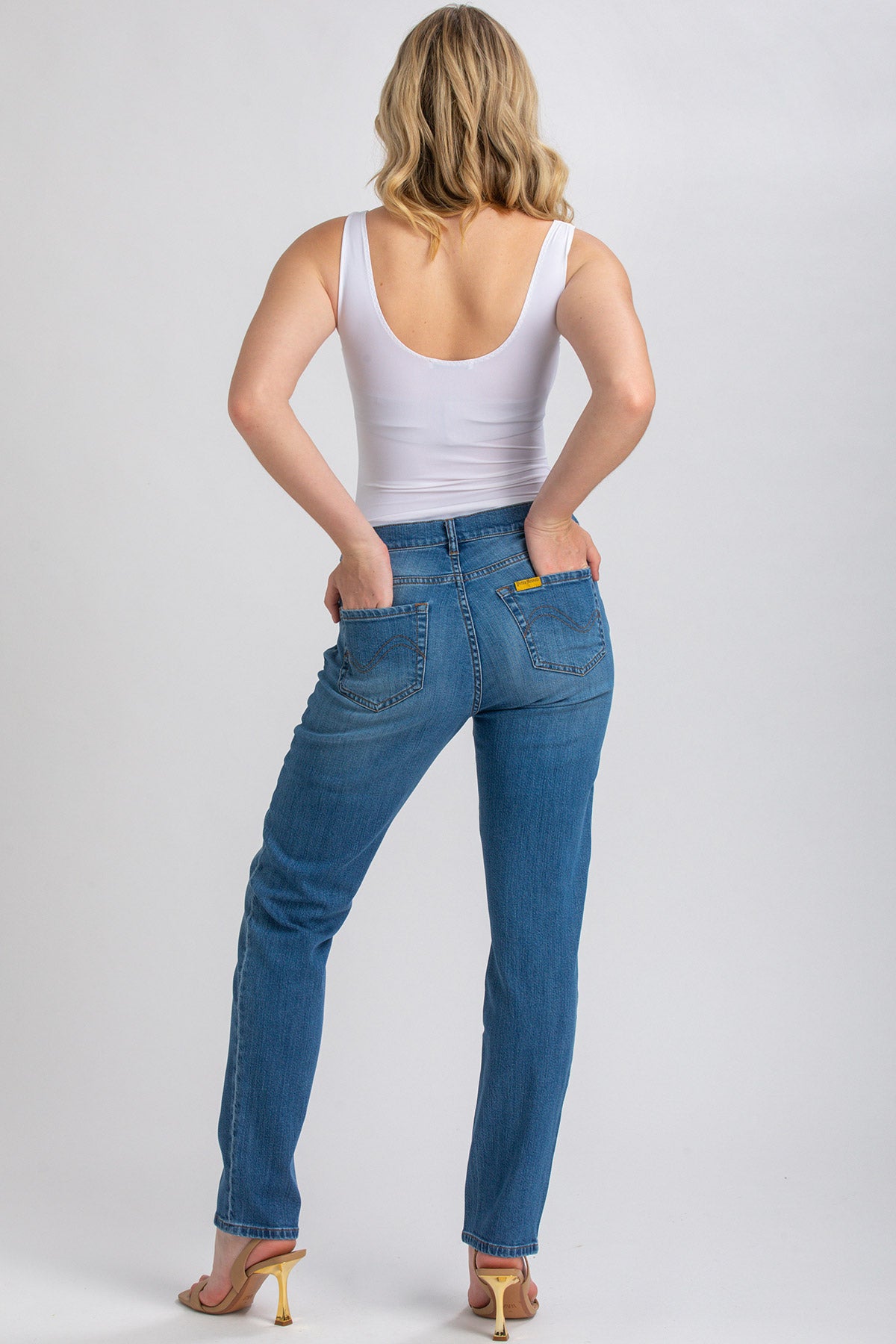 Donna di schiena con top bianco e jeans premaman blu, posa su sfondo neutro