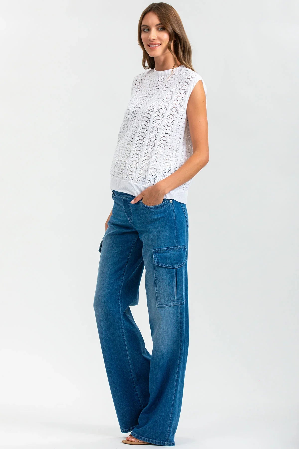 Donna con top premaman bianco traforato e pantaloni jeans larghi, abbigliamento gravidanza elegante