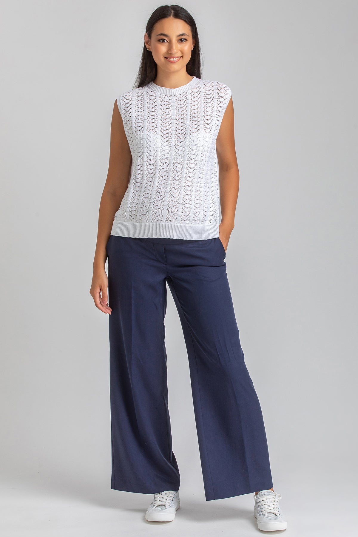Modella indossa top premaman bianco traforato e pantaloni blu ampi, look premaman elegante
