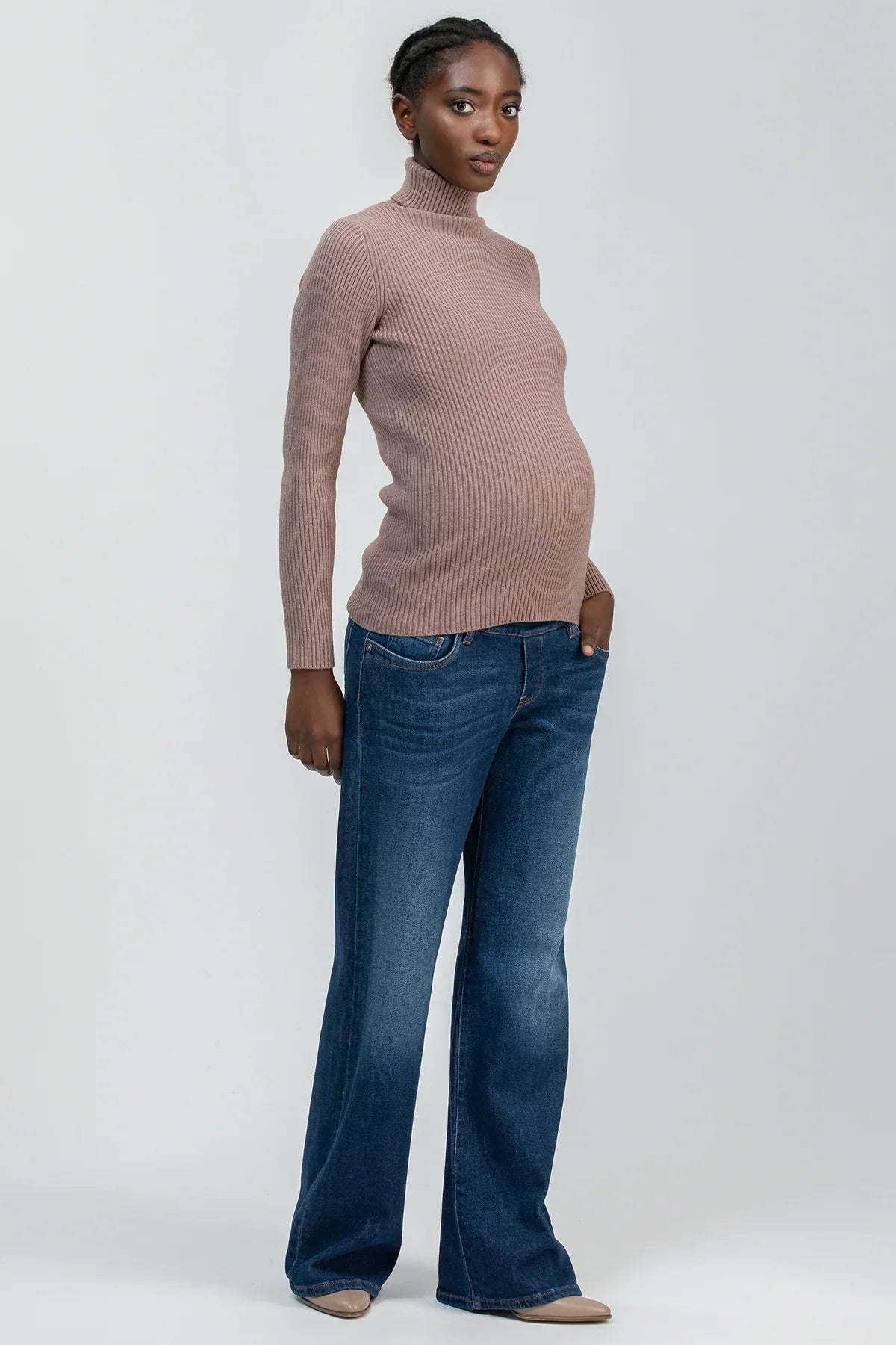Modella incinta con maglione premaman a collo alto rosa e jeans flare in denim