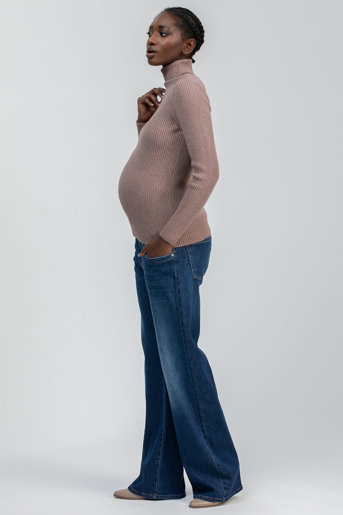 Donna incinta con maglione premaman a collo alto beige e jeans larghi blu, moda gravidanza elegante