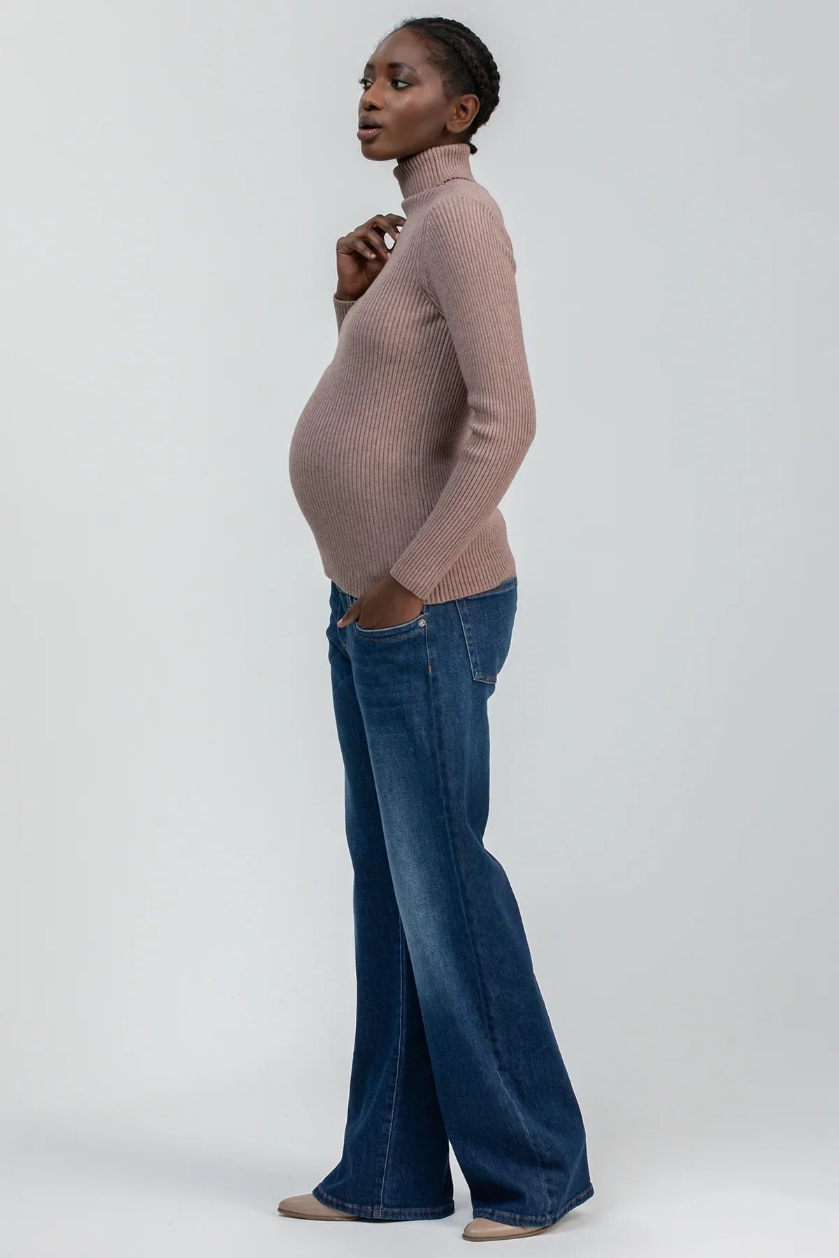 Modella incinta con maglione premaman a collo alto beige e jeans ampi, abbigliamento premaman elegante