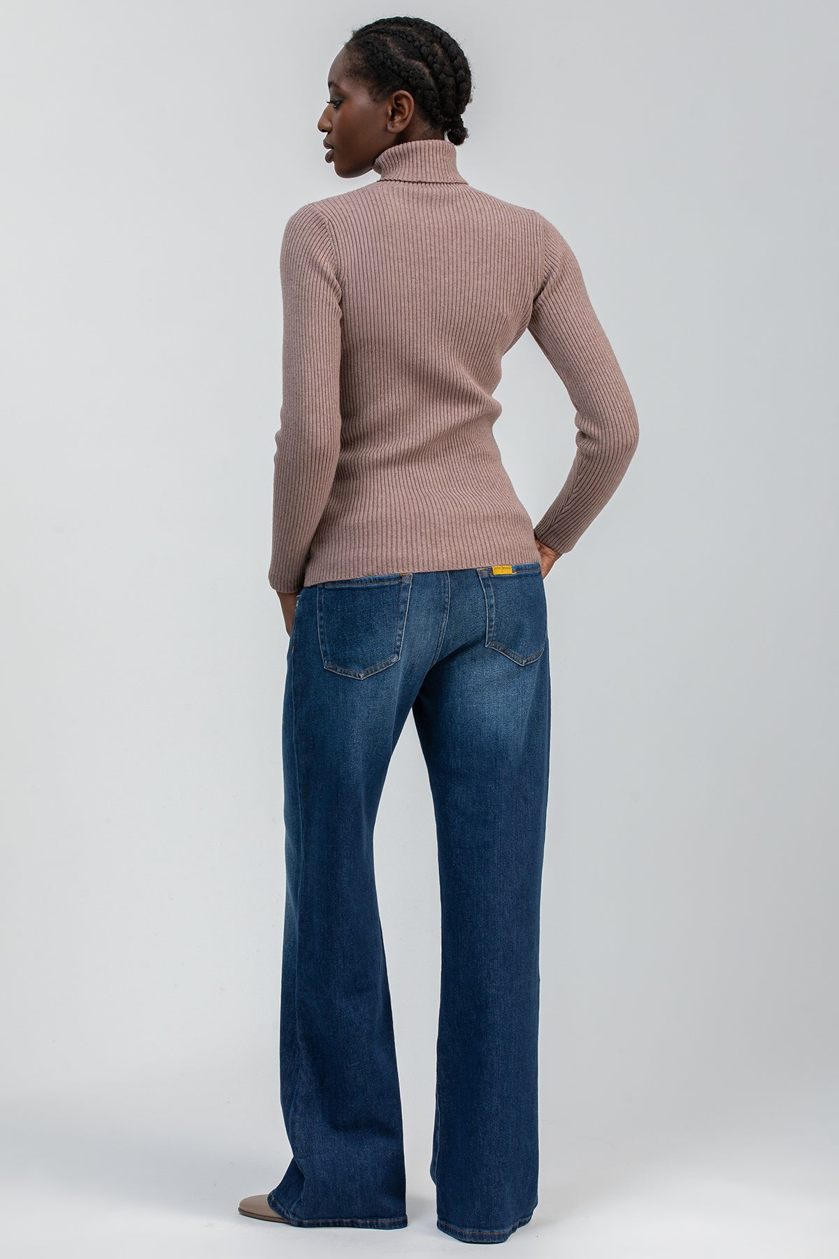 Donna di schiena con maglione premaman a coste color tortora e jeans ampi in denim