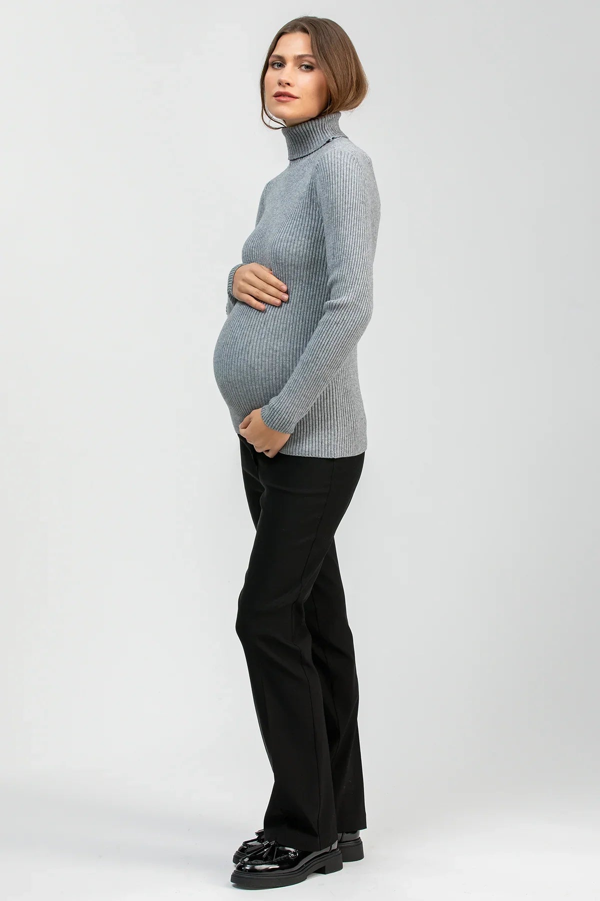 Donna incinta indossa maglione premaman grigio a collo alto e pantaloni neri eleganti.