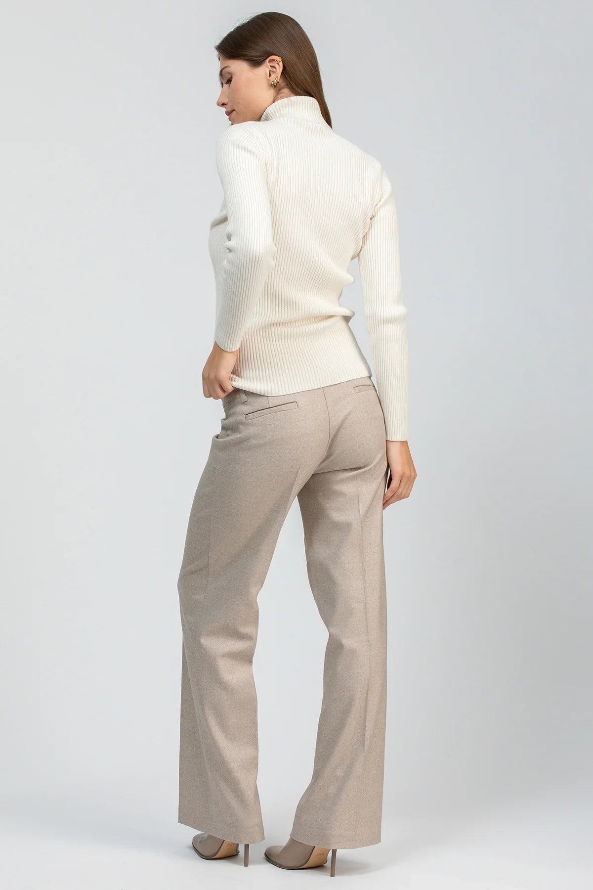 Modella con maglia premaman bianca a collo alto abbinata a pantaloni beige a gamba dritta