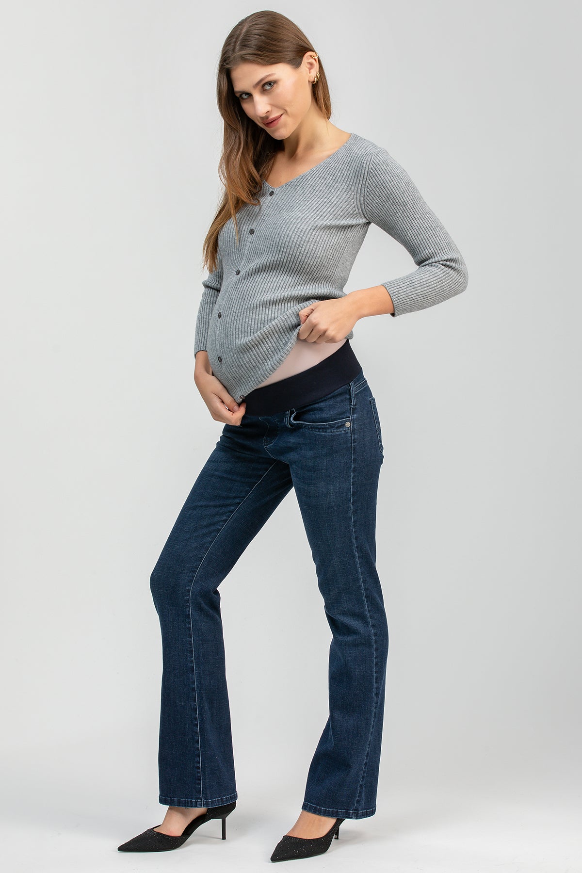 Donna incinta con maglia grigia e jeans premaman a zampa in studio, look casual elegante.