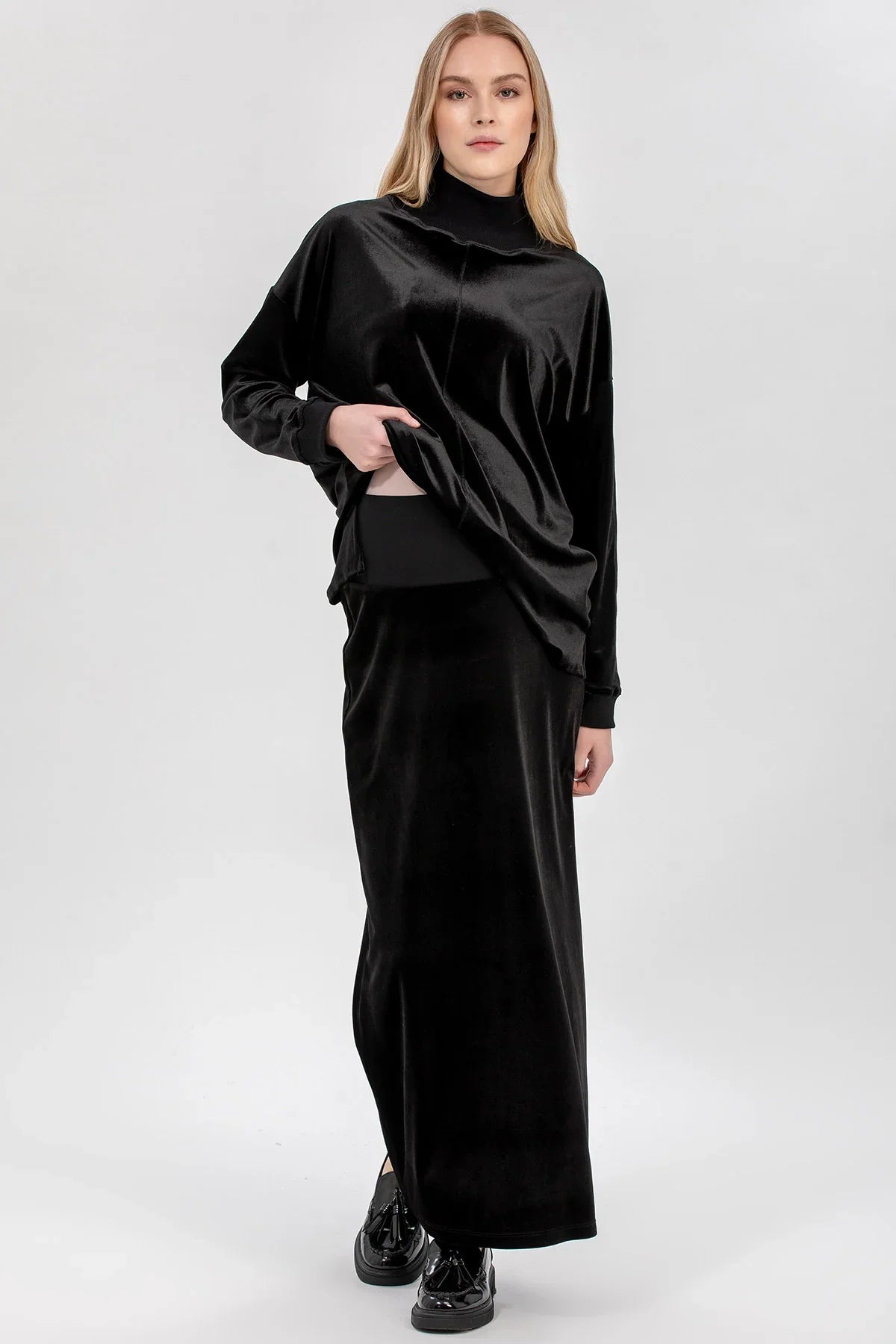 Modella indossa abbigliamento premaman elegante nero in velluto, maglia e gonna lunga.