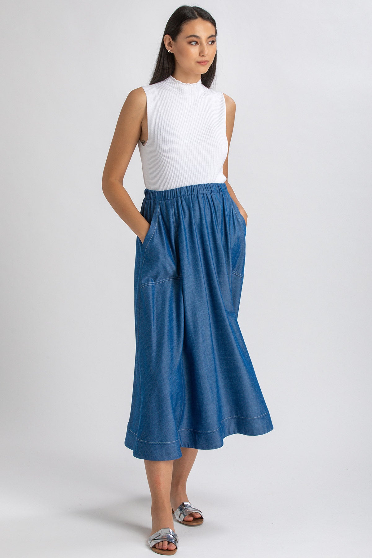 Donna con top bianco senza maniche e gonna lunga premaman in denim blu, sandali argento