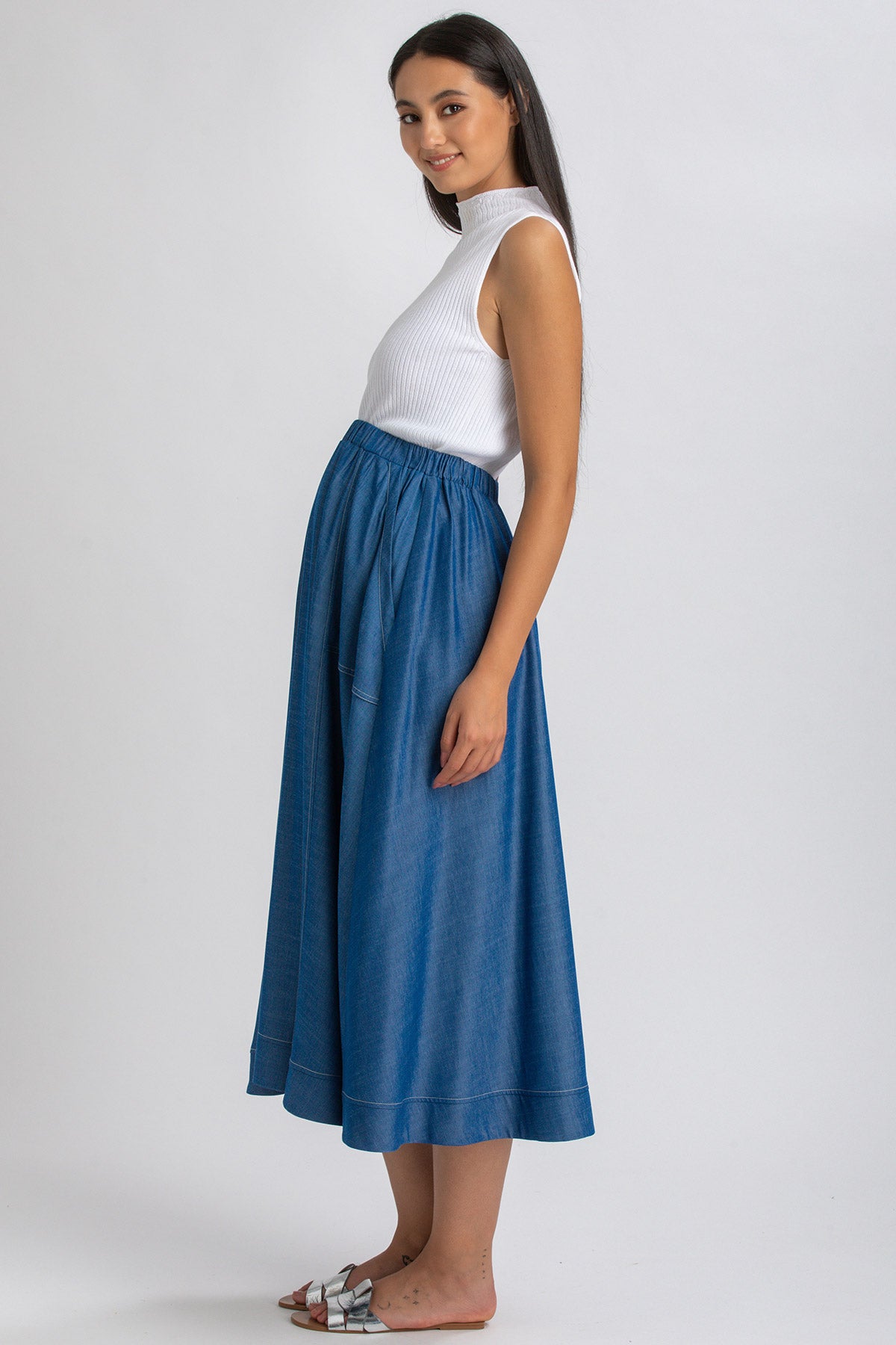 Donna incinta con gonna lunga in denim e top bianco senza maniche, look premaman elegante.