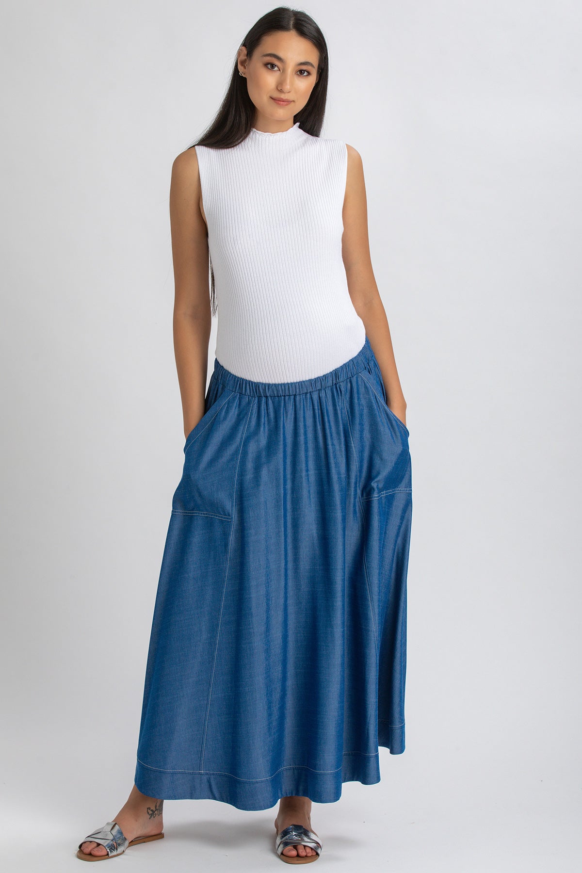 Donna incinta con gonna lunga premaman in denim blu e top bianco senza maniche
