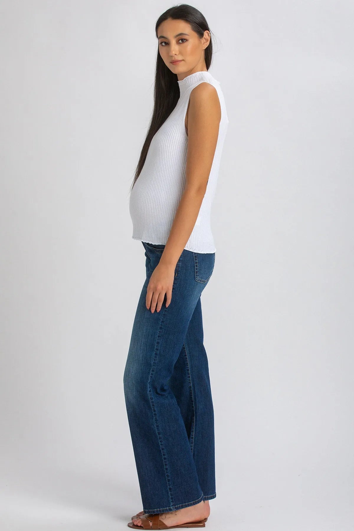 Donna incinta con top smanicato bianco premaman e jeans flare, look casual elegante.
