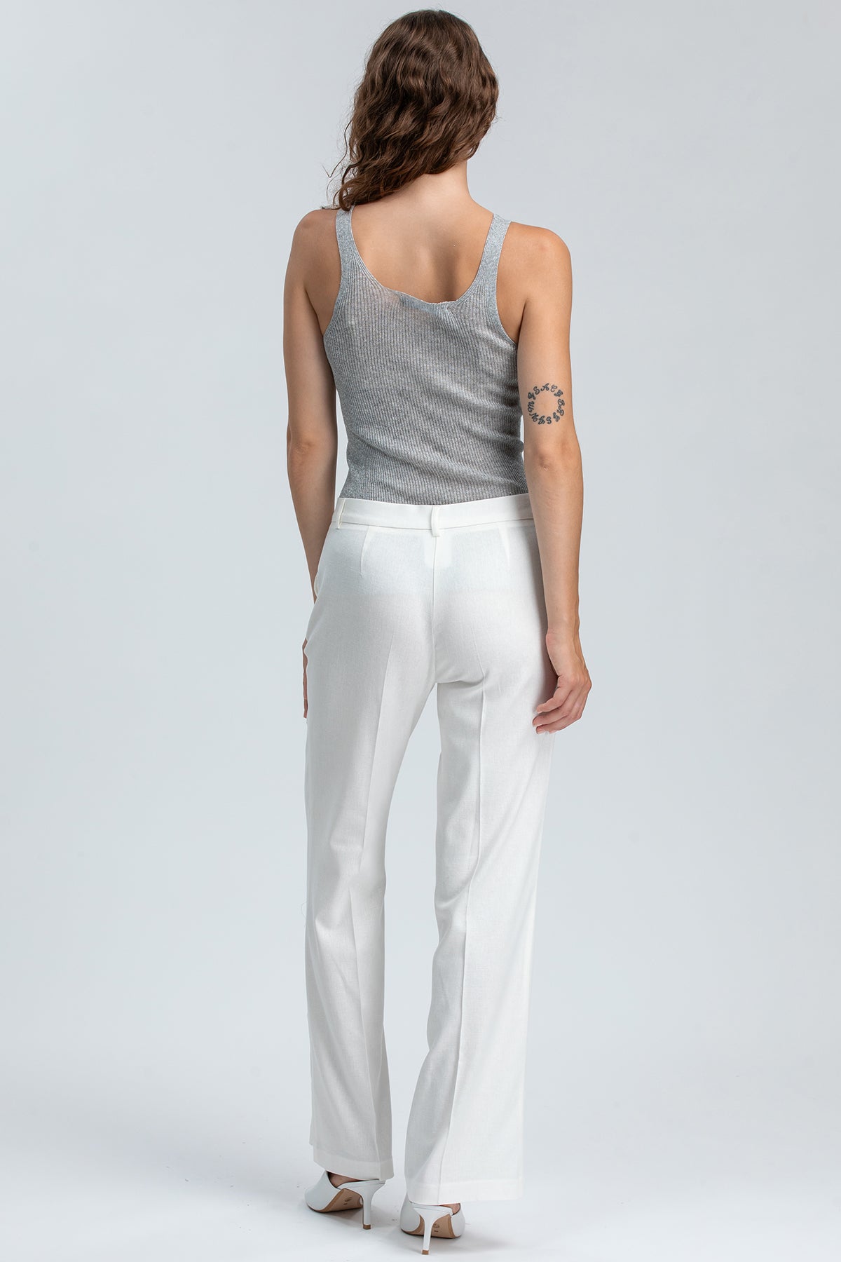 Donna di spalle con pantaloni premaman bianchi eleganti e top grigio, moda premaman elegante.