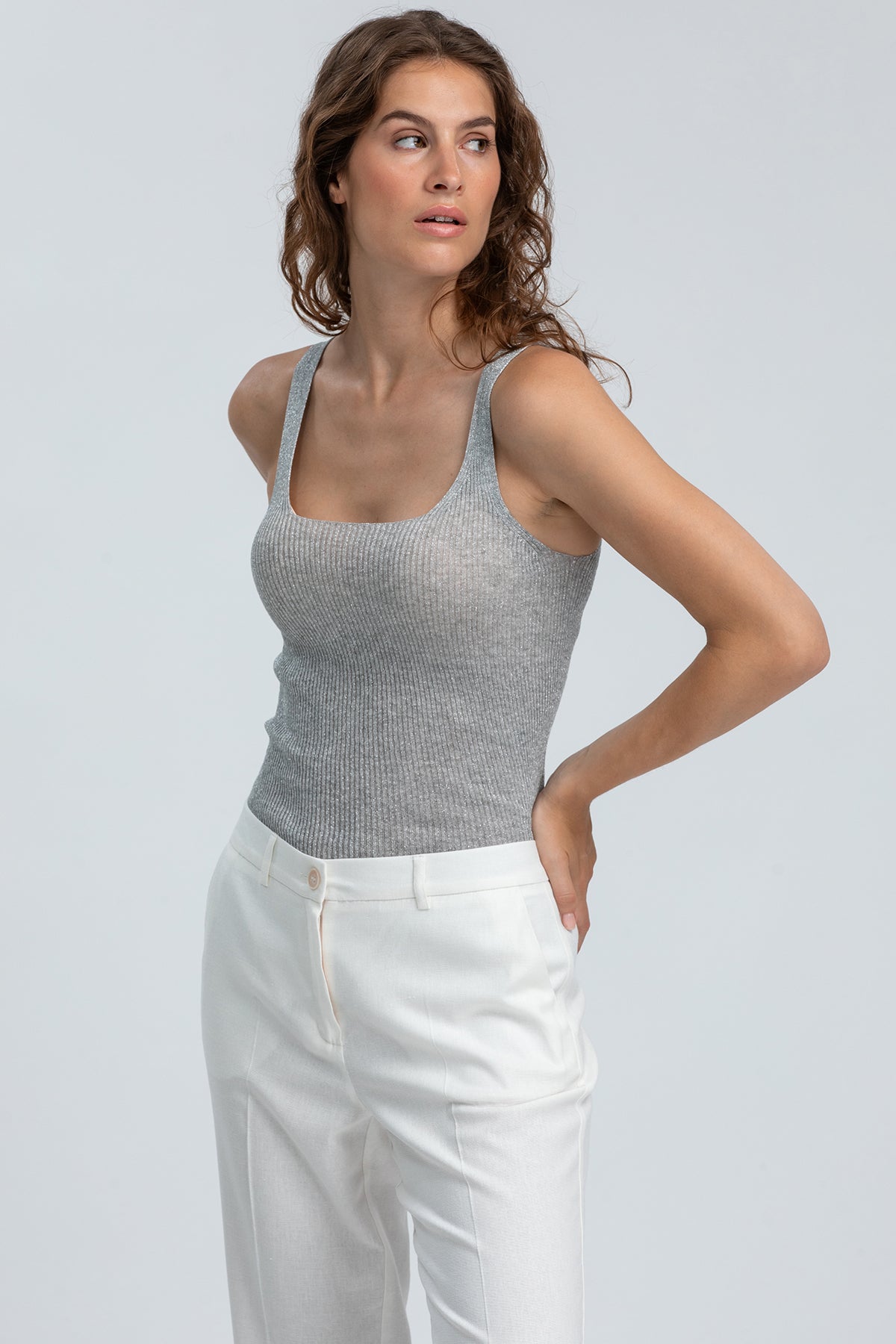 Modella indossa top premaman grigio senza maniche e pantaloni bianchi eleganti
