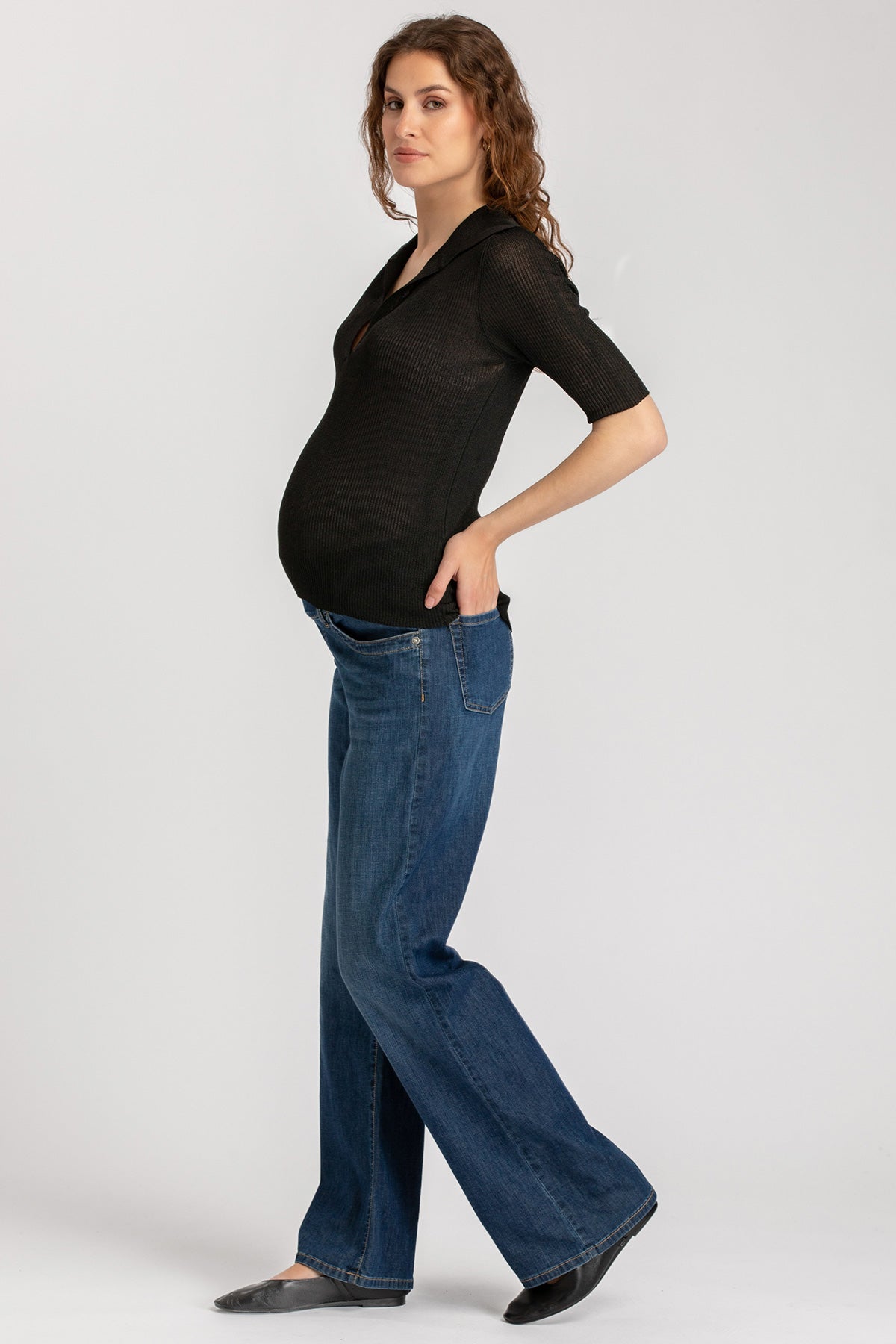 Donna incinta indossa top nero e jeans premaman su sfondo neutro, abbigliamento premaman casual