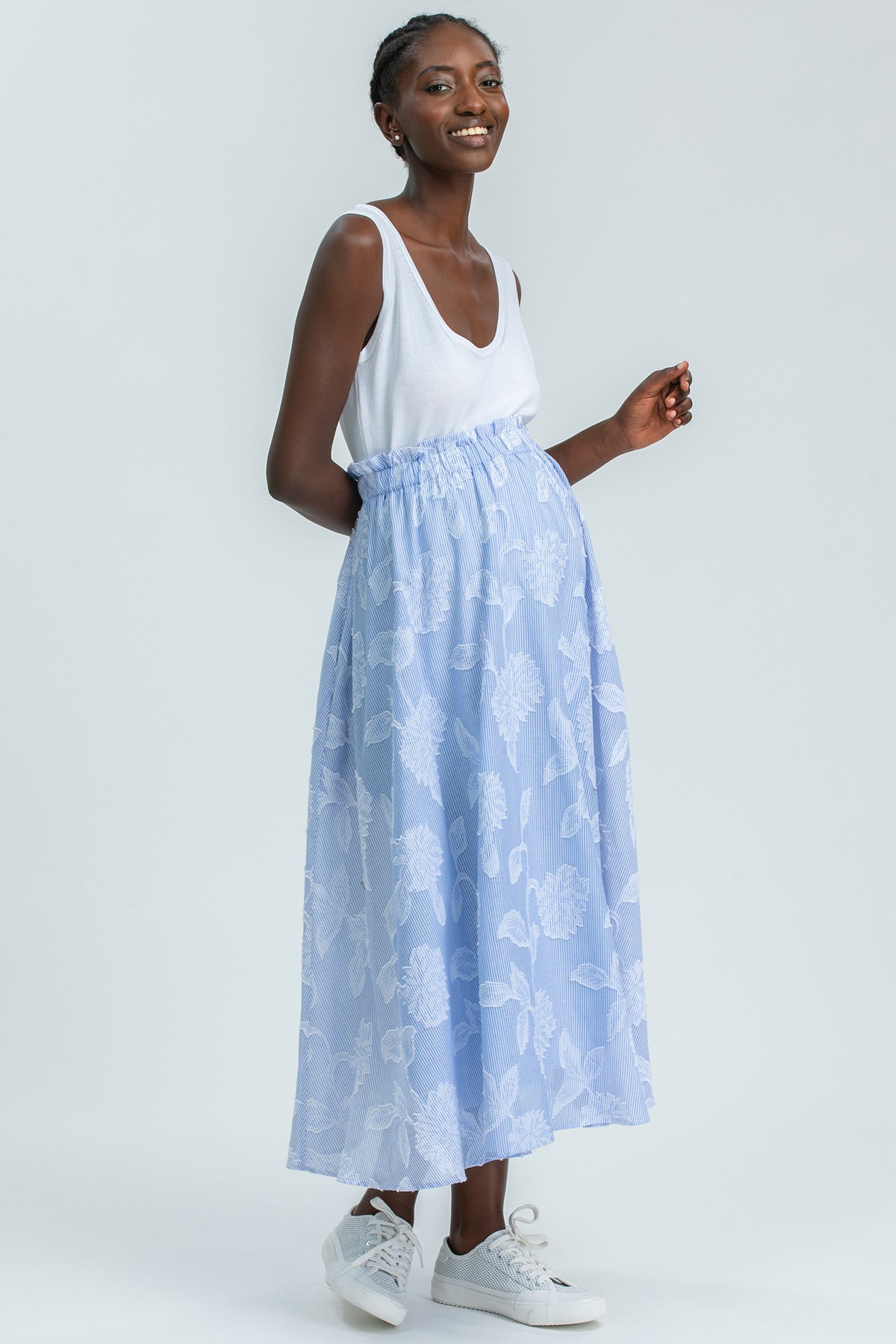 Modella indossa un abito premaman estivo bianco e azzurro con gonna lunga a fiori, stile casual elegante.