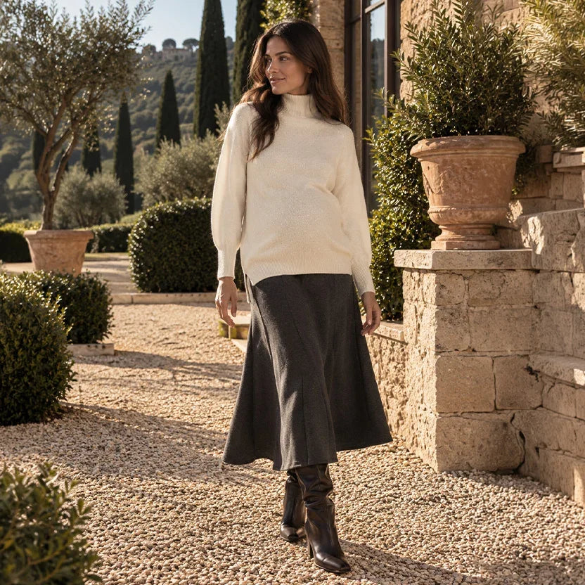 Donna incinta con maglione premaman color panna e gonna midi grigio scuro svasata, abbinati a stivali neri, nel cortile di una villa toscana.