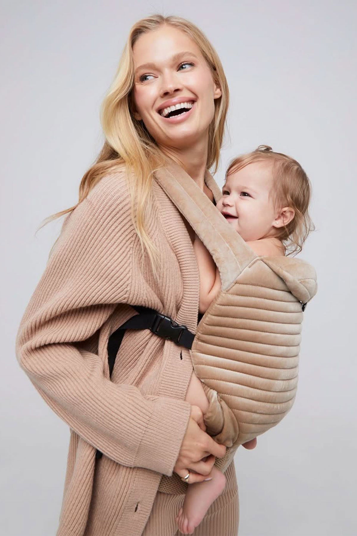 Mamma con abbigliamento premaman beige che porta il bambino in marsupio imbottito
