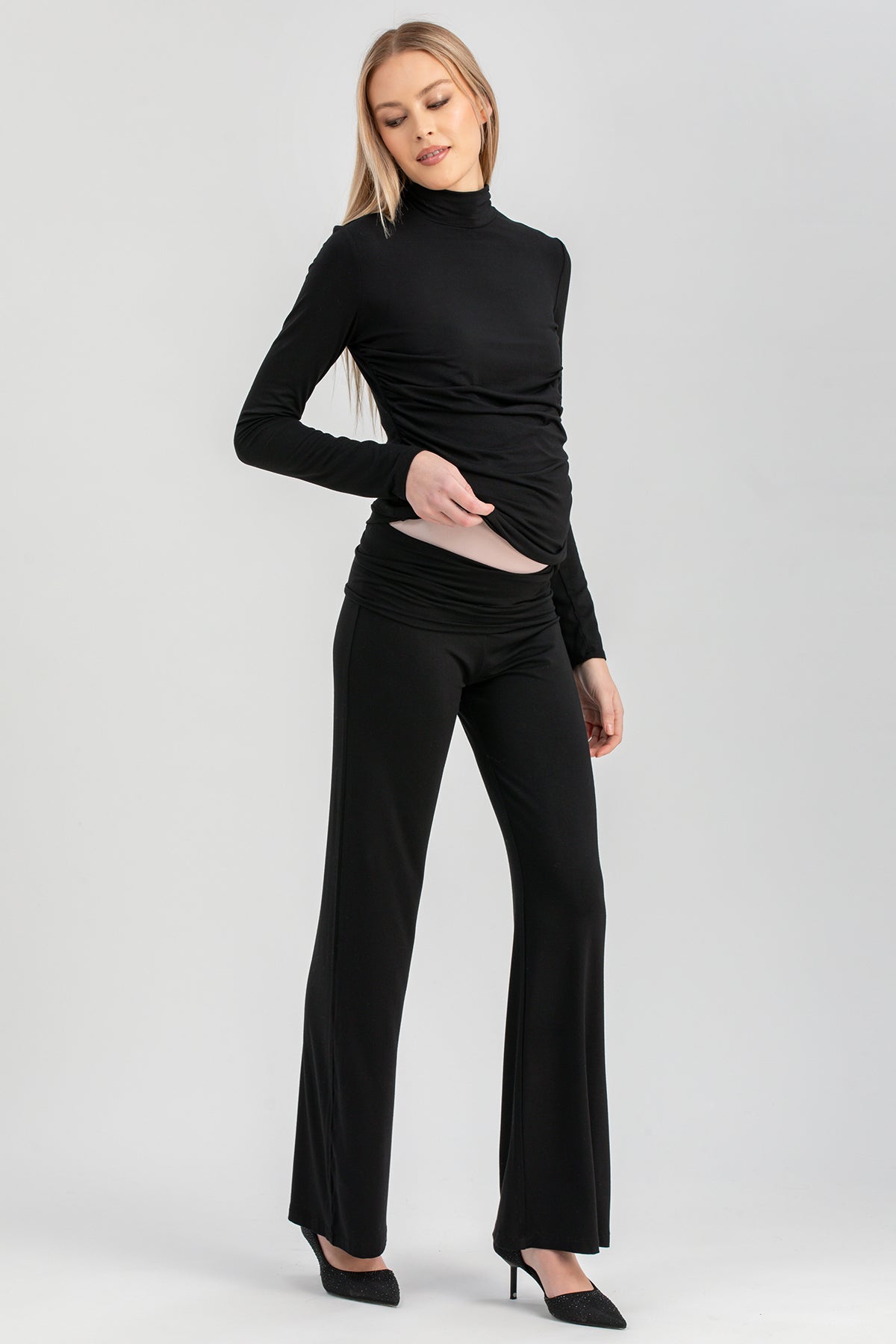 Modella indossa completo premaman nero elegante con pantaloni a zampa e maglia a collo alto